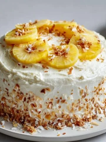 Homemade Coconut Pineapple Cake with cream cheese frosting, shredded coconut, and pineapple rings on a white kitchen table, shot from above