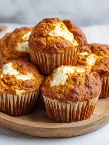 Freshly baked pumpkin cream cheese muffins on a white kitchen table, high-angle homemade photo with rustic Pumpkin Cream Cheese Muffins liners and crumbs.