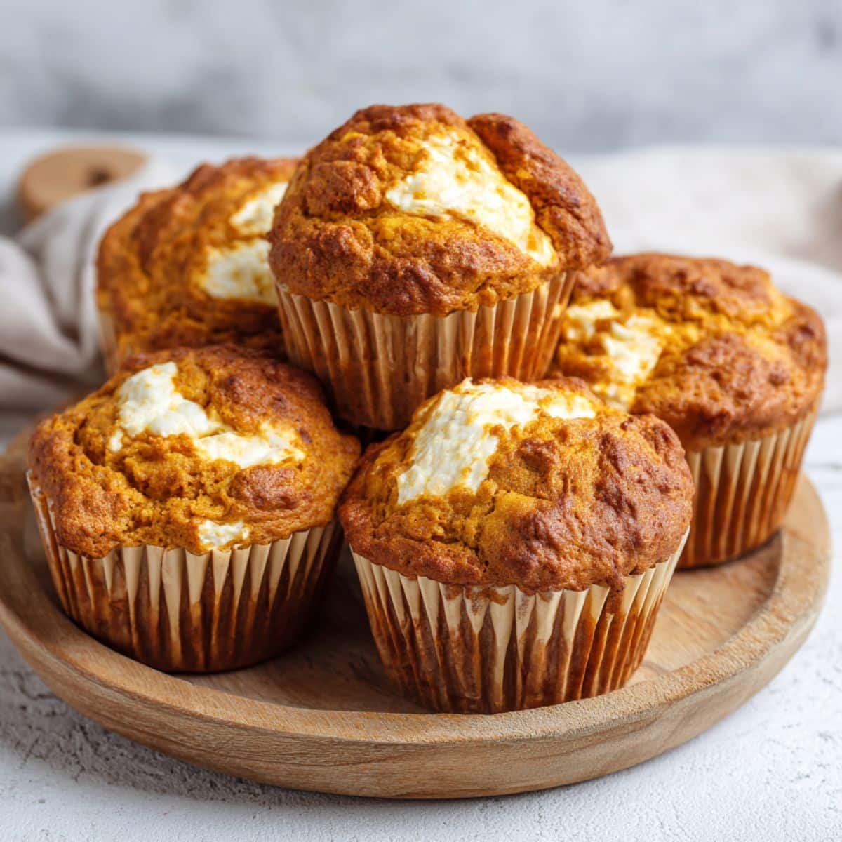 Freshly baked pumpkin cream cheese muffins on a white kitchen table, high-angle homemade photo with rustic Pumpkin Cream Cheese Muffins liners and crumbs.