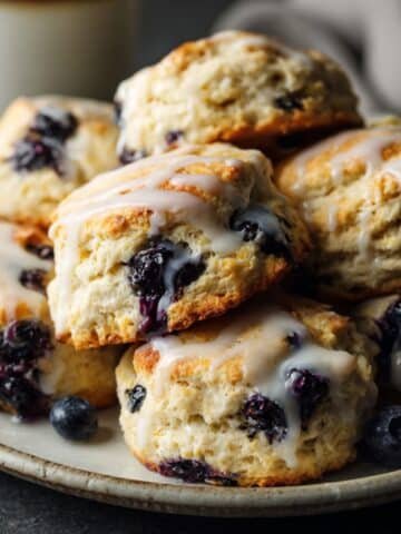 Homemade blueberry biscuits with golden tops and light lemon glaze on a white kitchen counter, photographed from above.