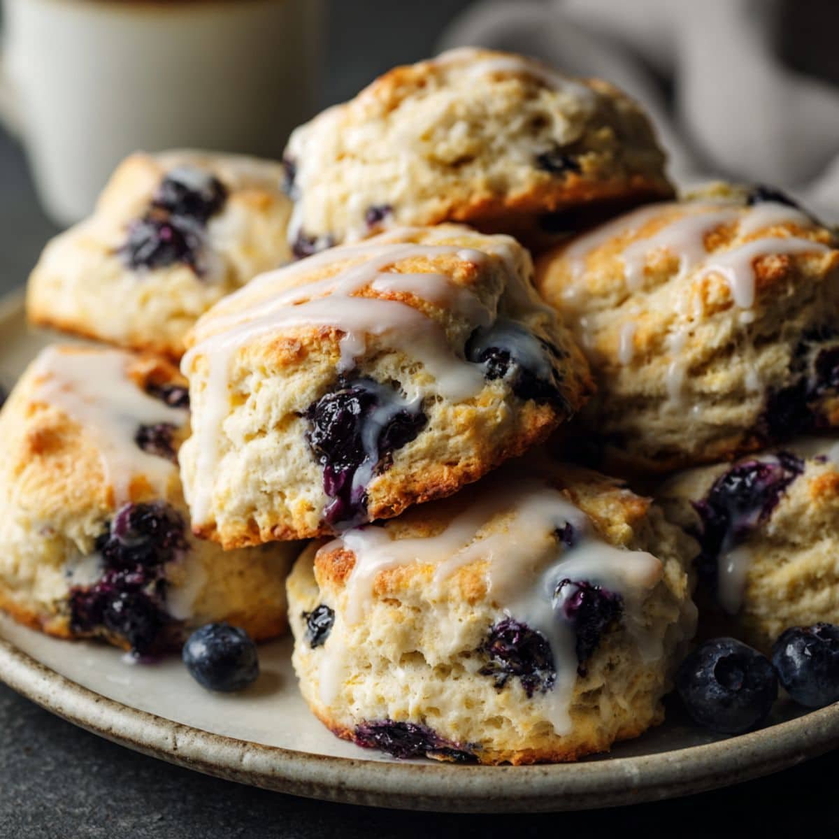 Homemade blueberry biscuits with golden tops and light lemon glaze on a white kitchen counter, photographed from above.
