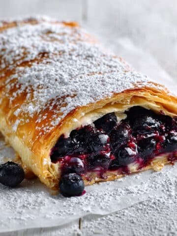 Homemade blueberry strudel on a white table with golden flaky pastry and blueberry filling