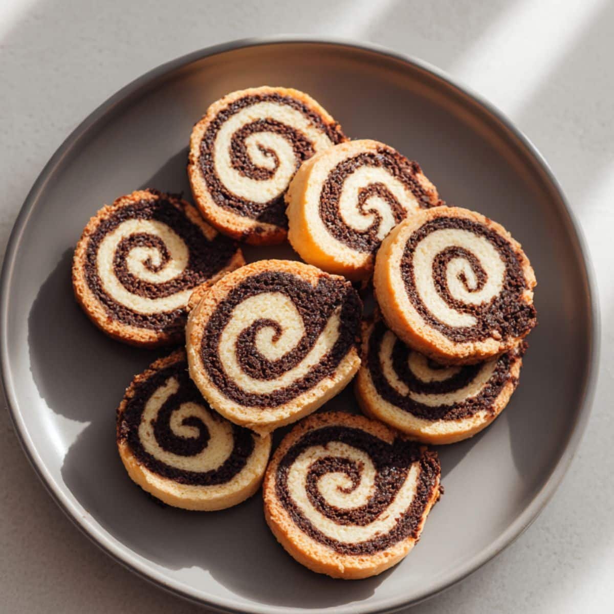A batch of homemade chocolate pinwheel cookies with chocolate and vanilla swirls on a white kitchen table, photographed from above.