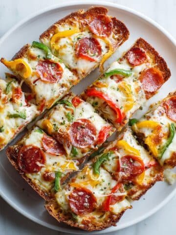 Homemade French bread pizza sliced on a white kitchen table with melted cheese and toppings, photographed from above