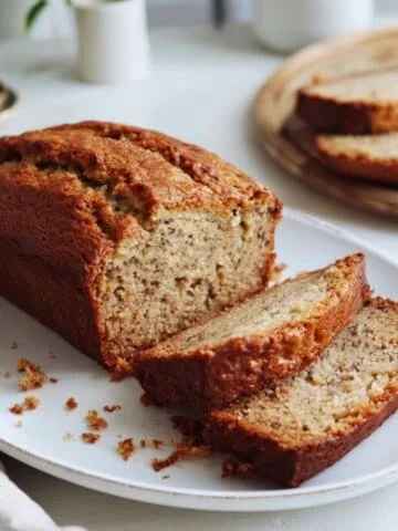 Homemade gluten-free banana bread loaf on a white kitchen table, sliced to show moist texture, photographed from above