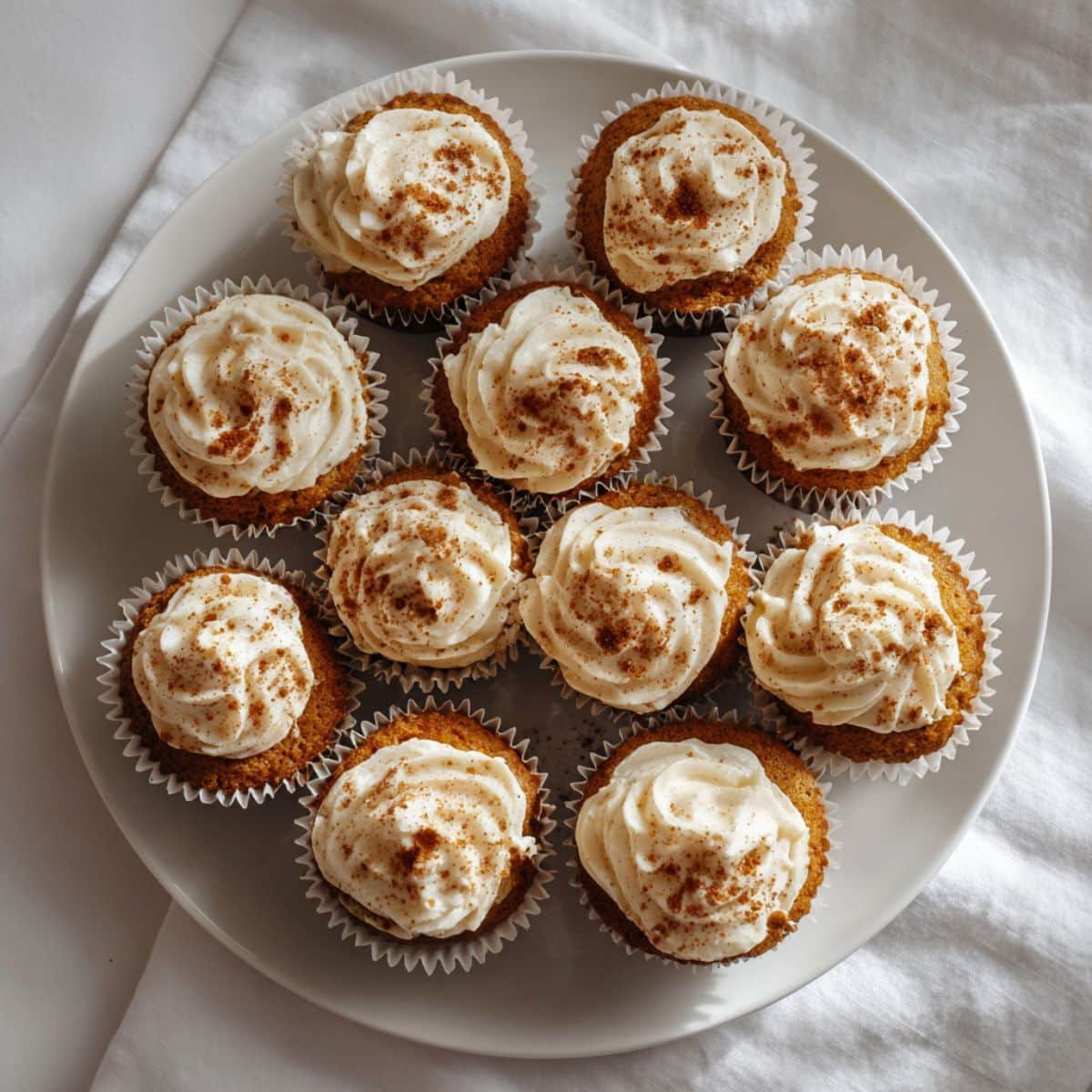 Homemade vegan pumpkin cupcakes with cream cheese frosting on a white kitchen table, shot from above