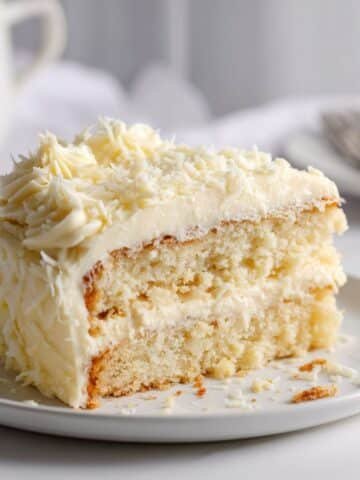 Homemade white chocolate cake with creamy frosting and white chocolate shavings on a white kitchen table
