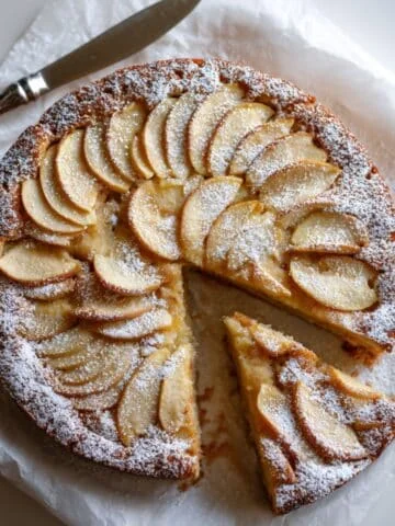 German apple cake on white table, one slice removed.