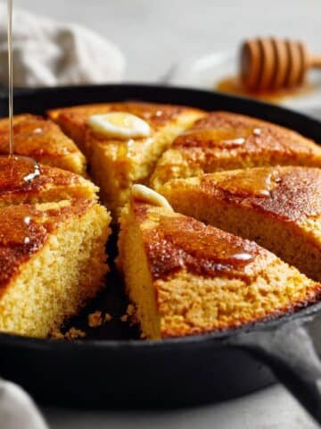 Freshly baked honey cornbread in cast iron skillet on white kitchen counter, top-down view