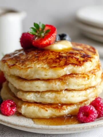 Fluffy keto pancakes with butter, syrup, and berries on white counter