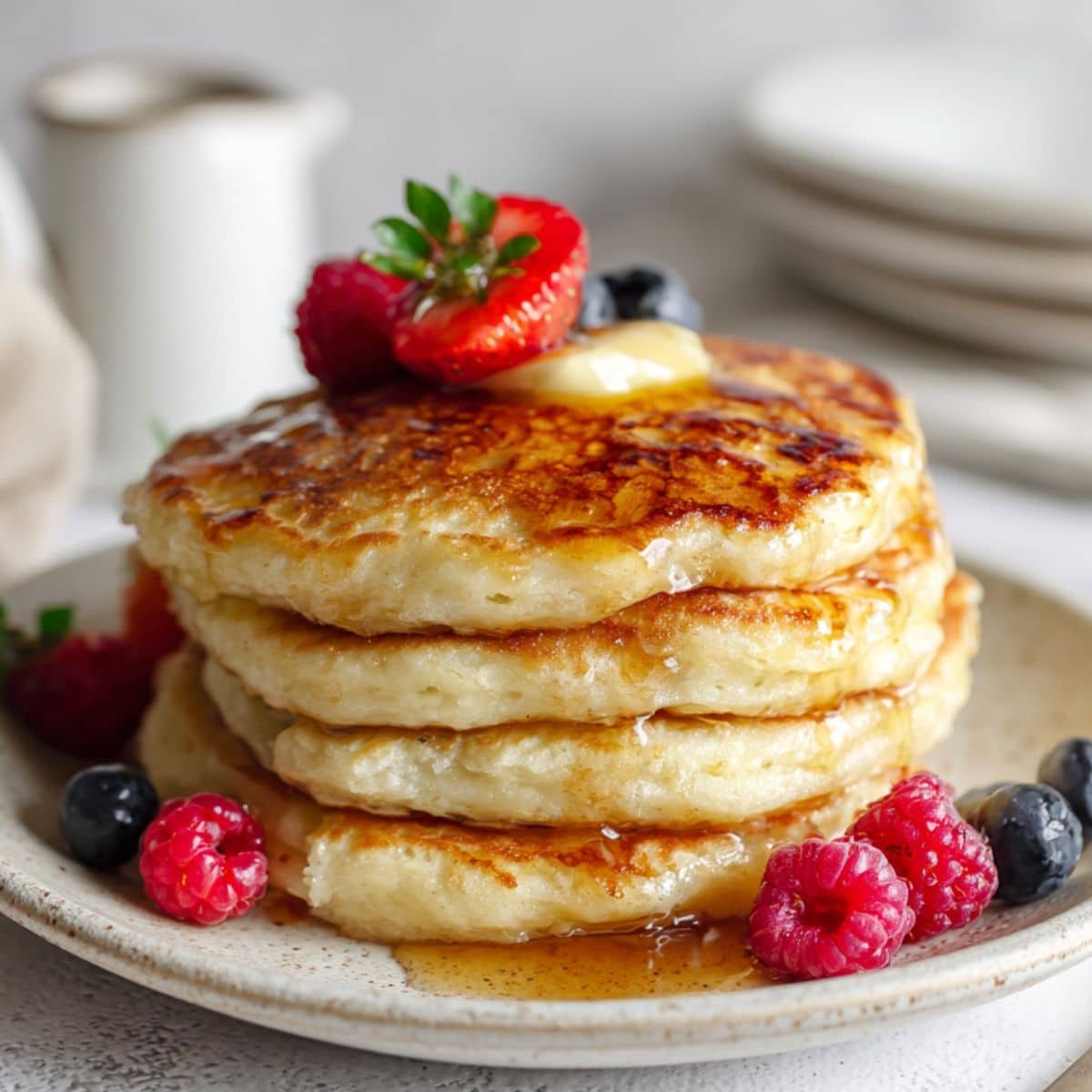 Fluffy keto pancakes with butter, syrup, and berries on white counter