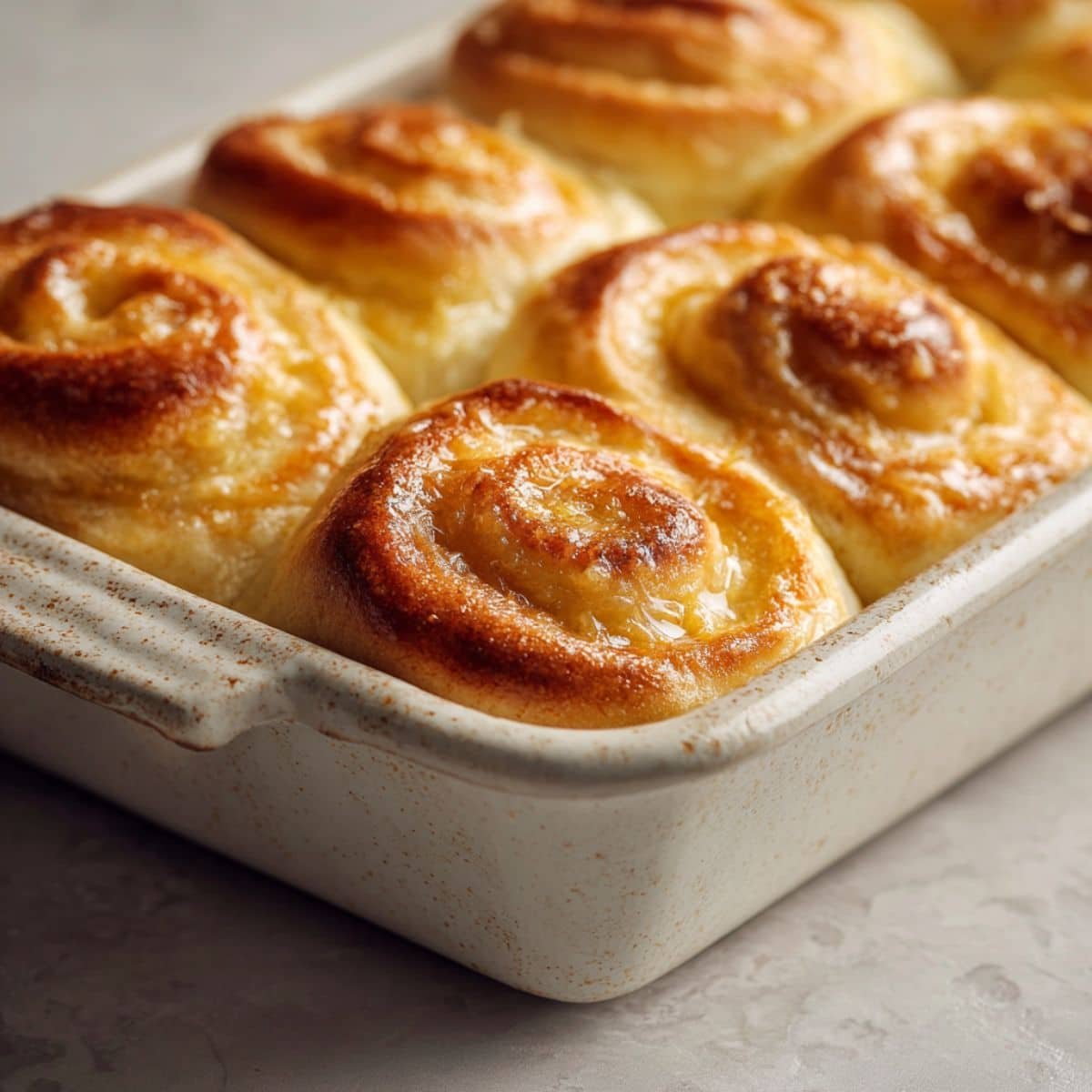 Freshly baked Lion House rolls on a white kitchen counter, golden brown spiral dinner rolls brushed with butter