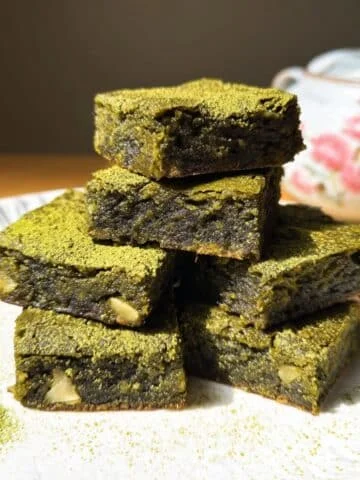 Fudgy matcha brownies cut into squares, dusted with powdered sugar on a white kitchen counter