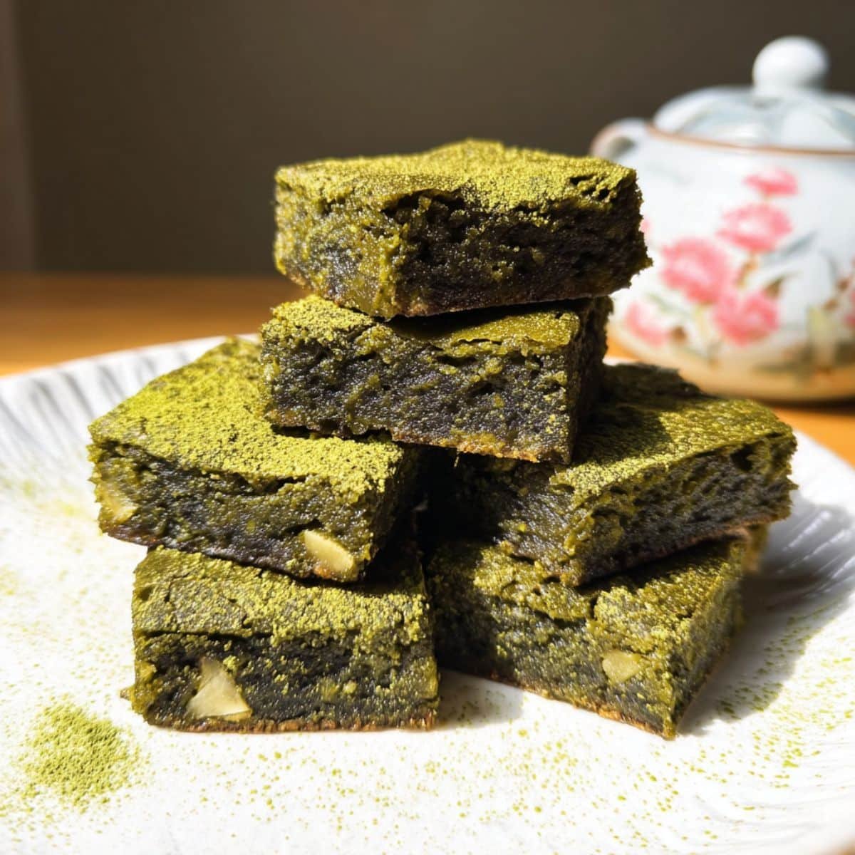 Fudgy matcha brownies cut into squares, dusted with powdered sugar on a white kitchen counter