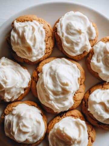Homemade pumpkin cookies with cream cheese icing on a white kitchen table, top-down view with rustic, cozy feel.