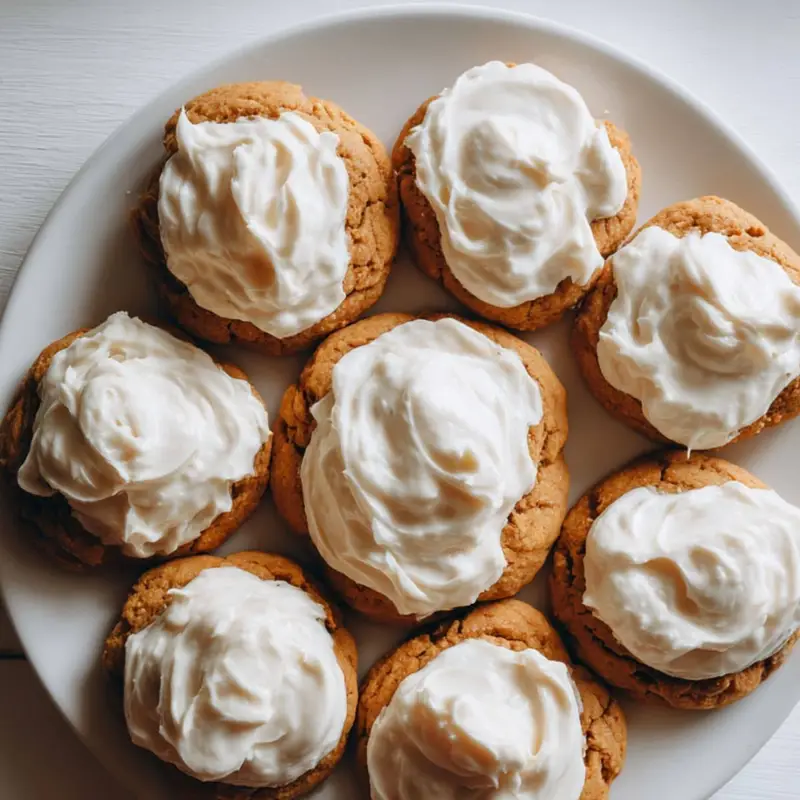 Homemade pumpkin cookies with cream cheese icing on a white kitchen table, top-down view with rustic, cozy feel.