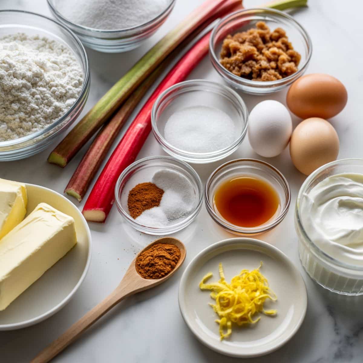 All ingredients for rhubarb cake laid out on a white kitchen table, photographed from above.