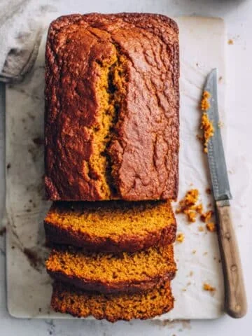 Homemade vegan pumpkin banana bread loaf sliced on a white kitchen table, shot from above