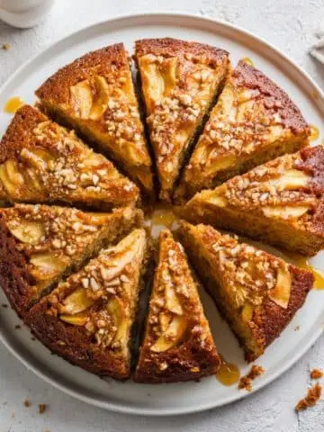 Homemade apple honey cake sliced on a white kitchen table, showing its moist crumb and honey glaze in natural daylight.