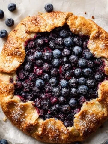 Homemade blueberry crostata with rustic golden crust and bubbling blueberry filling on a white kitchen table, photographed from above.