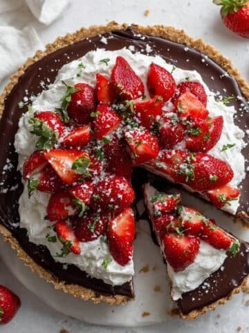 Homemade chocolate strawberry pie with a slice cut out, topped with whipped cream and fresh strawberries on a white kitchen counter.