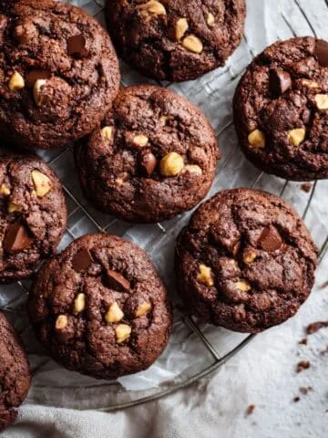 Homemade chocolate hazelnut cookies cooling in kitchen table, with crumbs and hazelnuts scattered around for a cozy homemade feel.
