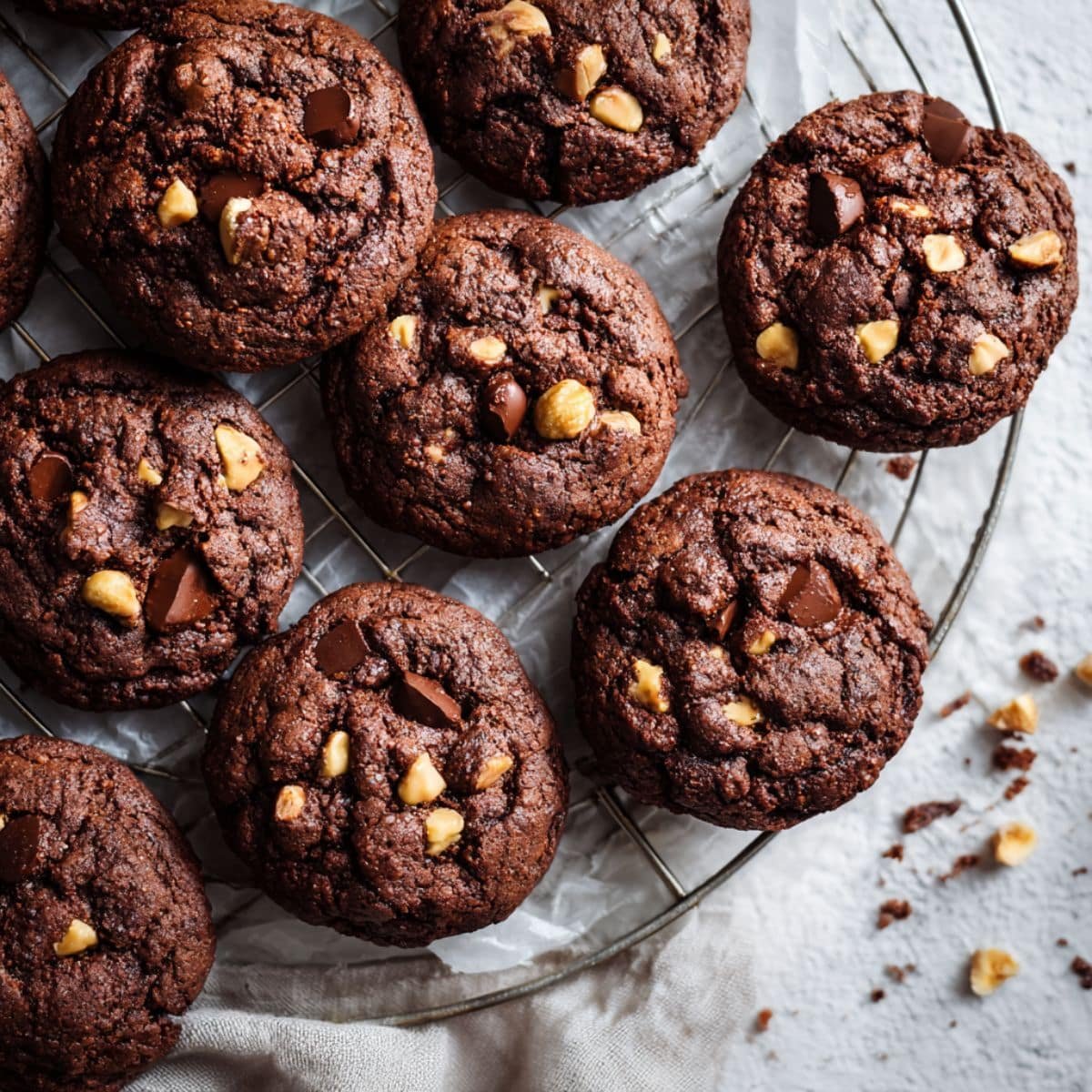 Homemade chocolate hazelnut cookies cooling in kitchen table, with crumbs and hazelnuts scattered around for a cozy homemade feel.