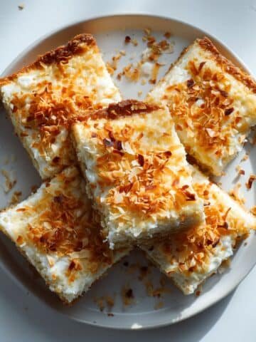 Homemade coconut cream pie bars with creamy coconut filling and toasted coconut on top, served on a white kitchen table.