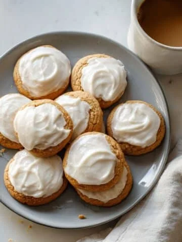 Homemade iced pumpkin cookies with creamy frosting on a white kitchen table, shot from above.
