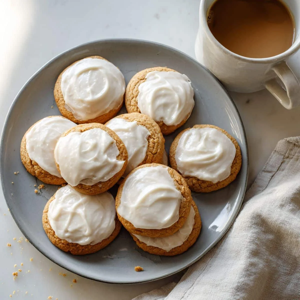 Homemade iced pumpkin cookies with creamy frosting on a white kitchen table, shot from above.