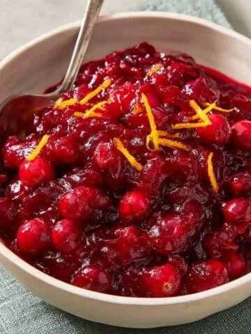 Homemade cranberry sauce with fresh cranberries and orange zest served in a white bowl on a white kitchen table, photographed from above.