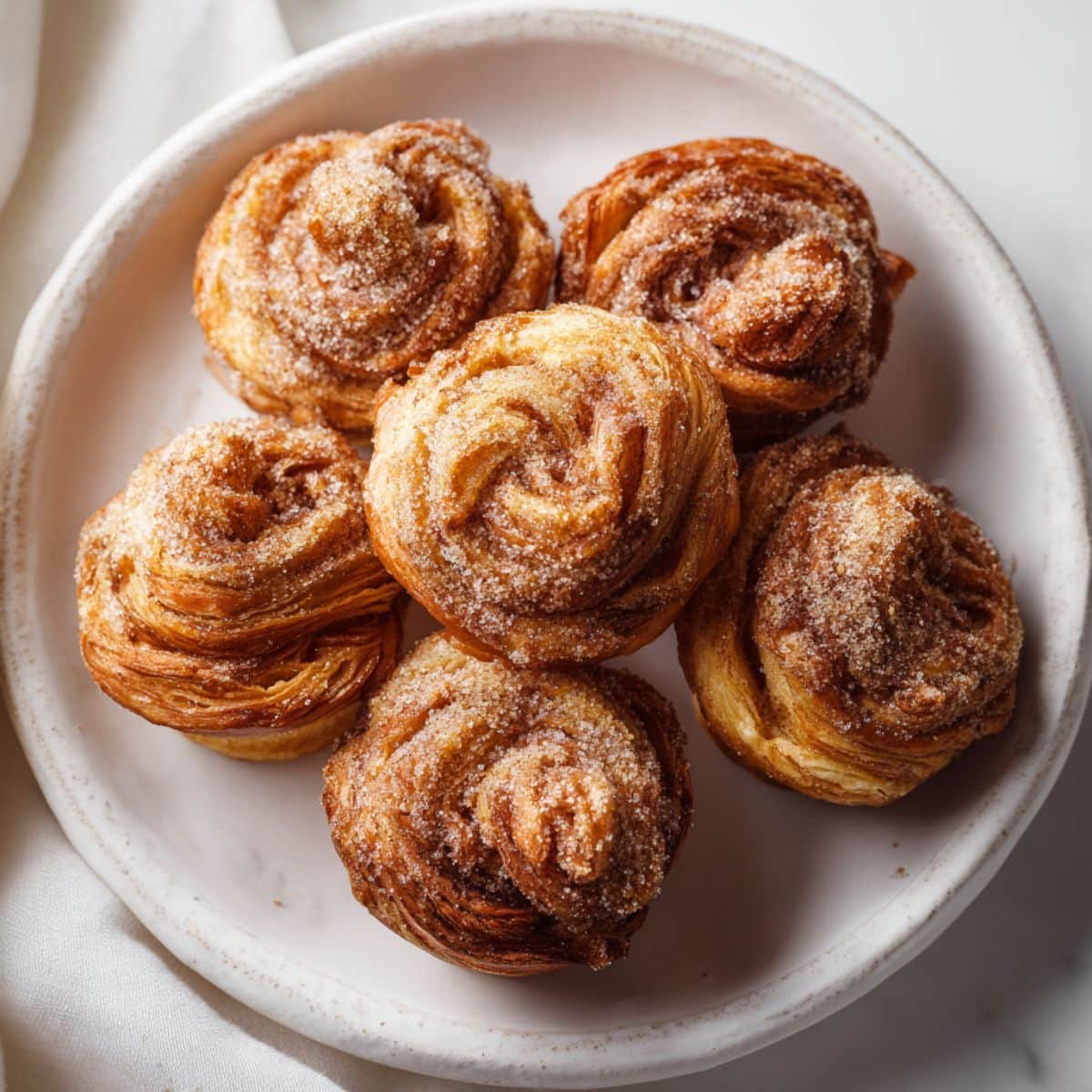 Freshly baked apple butter cruffins coated in cinnamon sugar, on a white kitchen table.