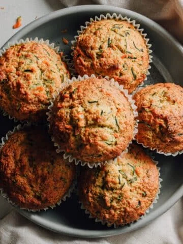 Freshly baked zucchini and carrot muffins cooling on a white kitchen counter, shot from above with natural lighting.