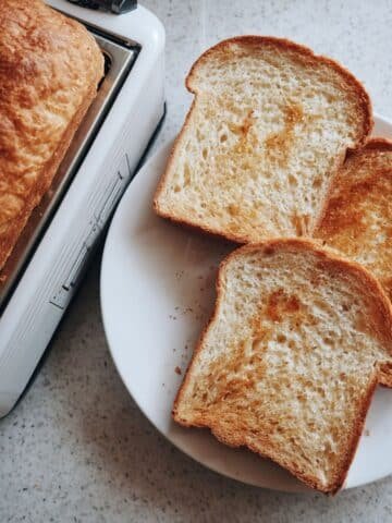 Homemade loaf of bread with slices of golden toast on a white kitchen table, photographed from above.