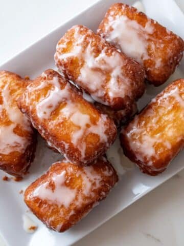 Freshly glazed homemade buttermilk bar donuts with vanilla icing drips on a white kitchen counter.