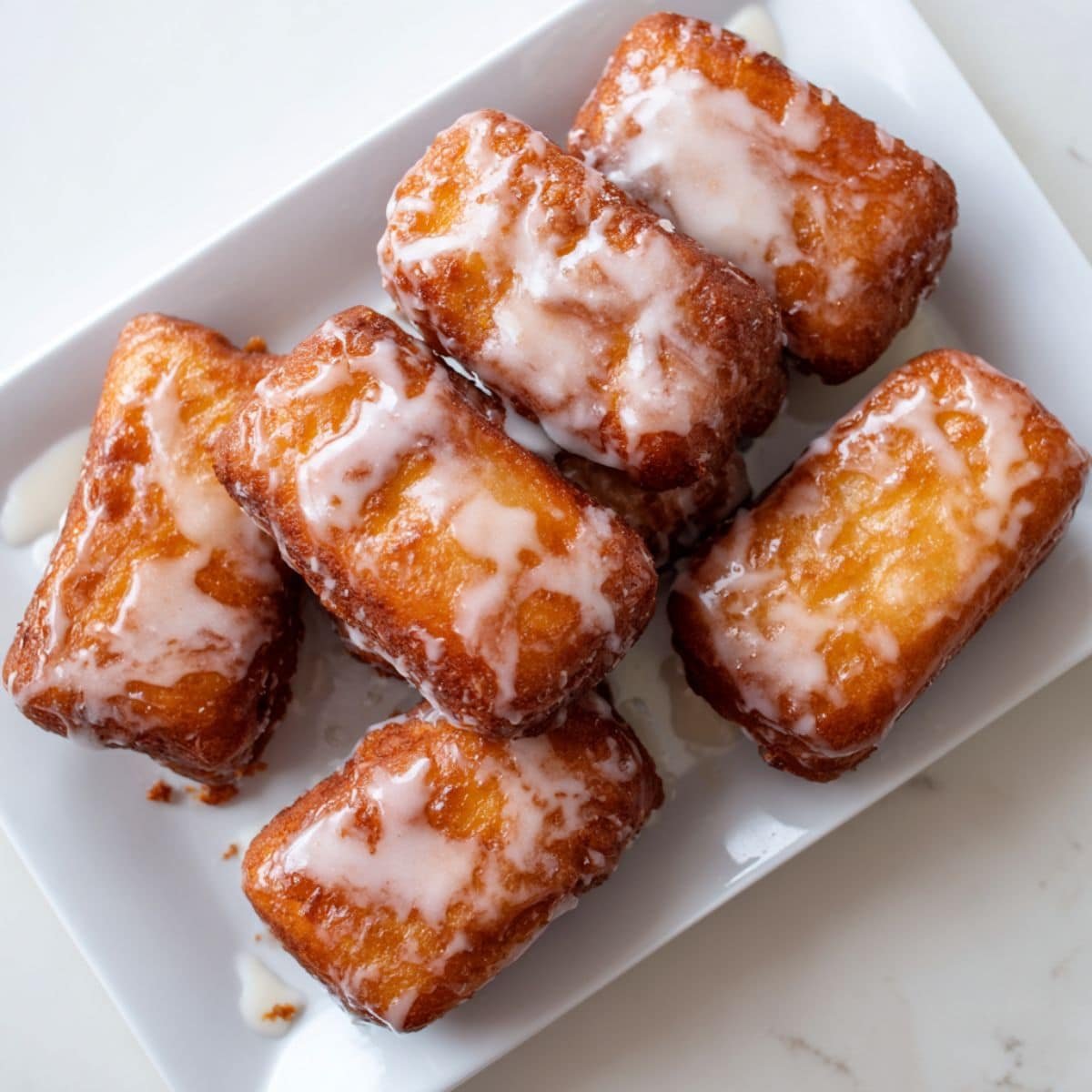 Freshly glazed homemade buttermilk bar donuts  with vanilla icing drips on a white kitchen counter.