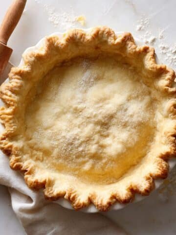 Golden flaky sour cream pie crust on a white kitchen counter with a rolling pin and flour dust, captured from above in natural light.