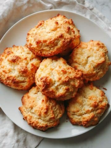 Homemade keto biscuits with golden tops cooling on a white kitchen counter, photographed from above in natural daylight.