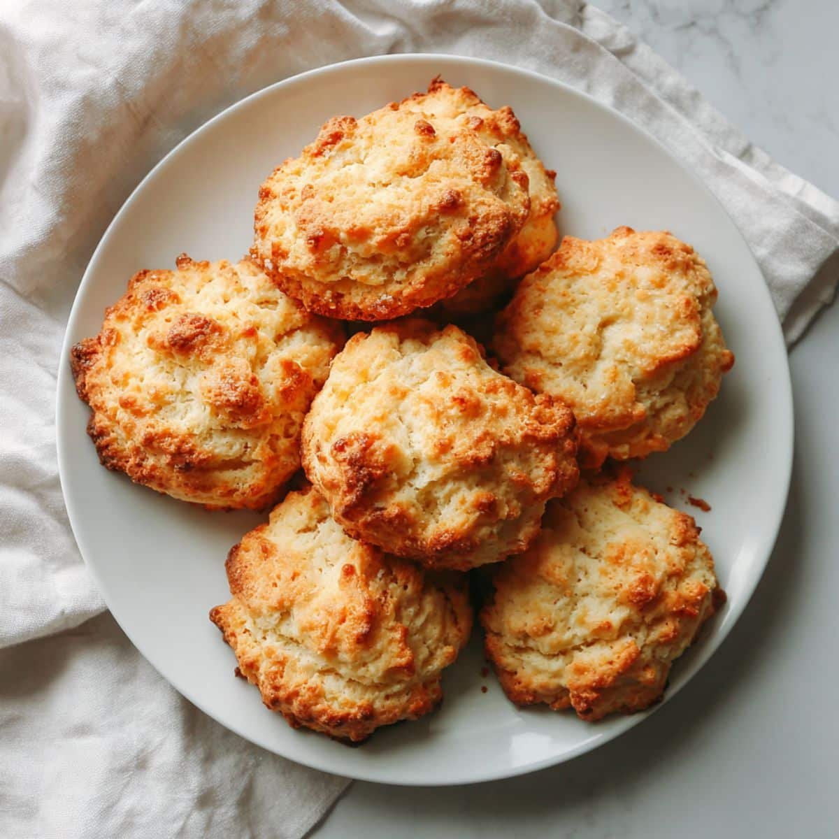 Homemade keto biscuits with golden tops cooling on a white kitchen counter, photographed from above in natural daylight.