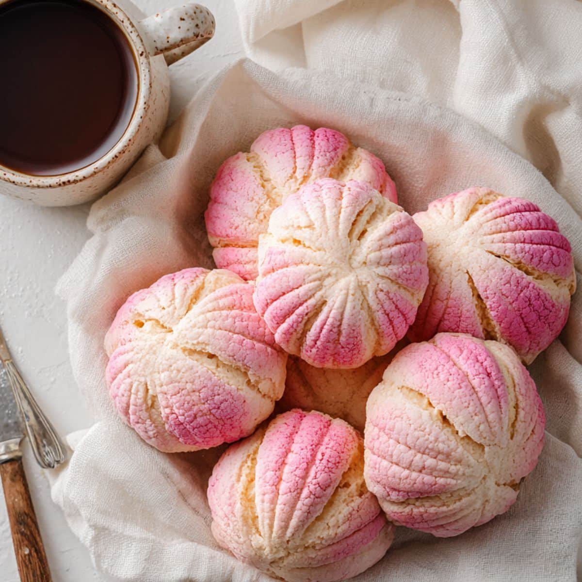 Freshly baked pink concha bread on a white kitchen counter with coffee.