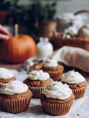 Freshly frosted homemade pumpkin cupcakes on a white kitchen table.