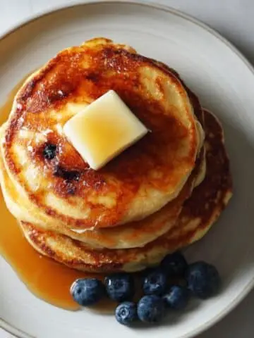 frozen pancakes stacked on a white plate with butter and syrup, photographed from above on a white kitchen table