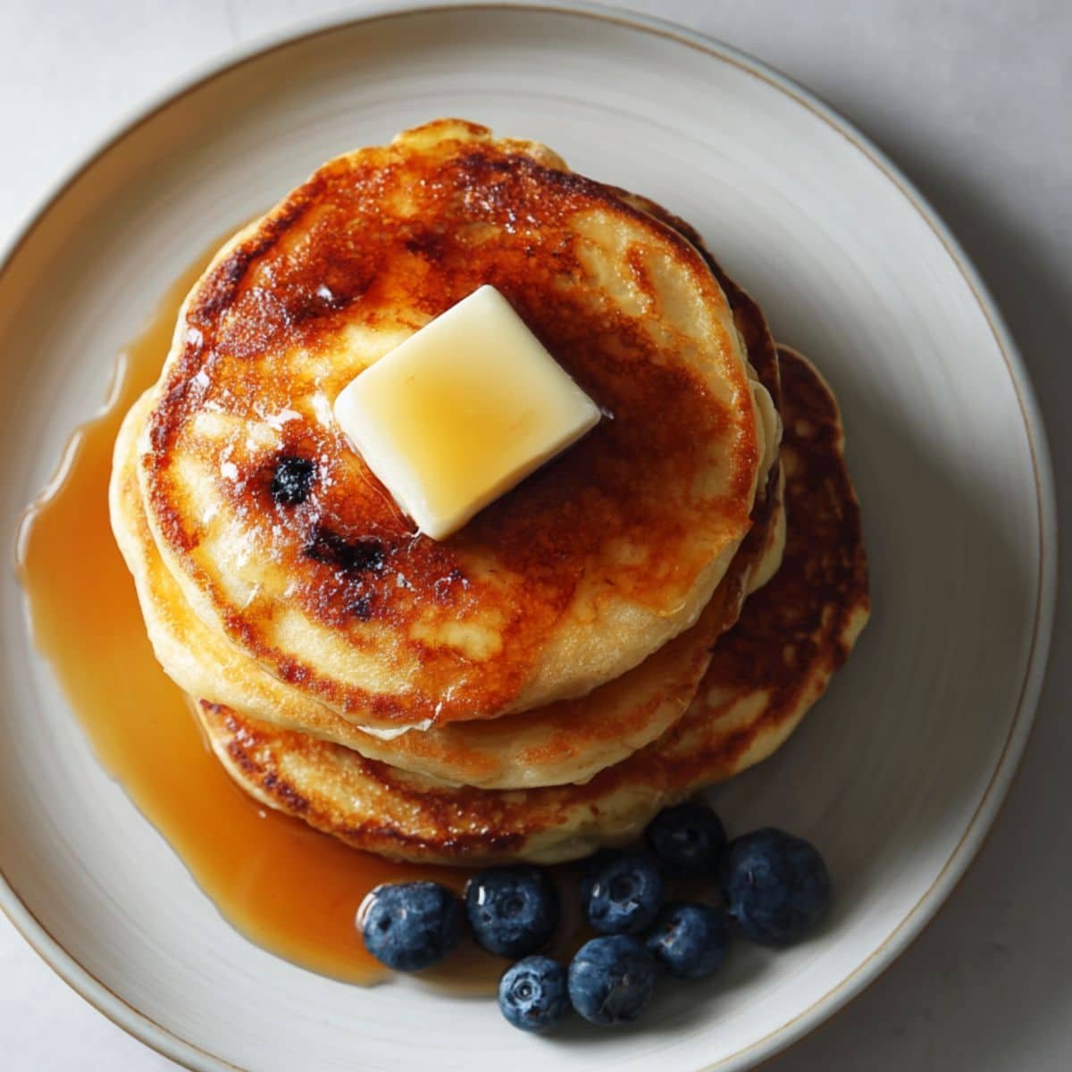 frozen pancakes stacked on a white plate with butter and syrup, photographed from above on a white kitchen table