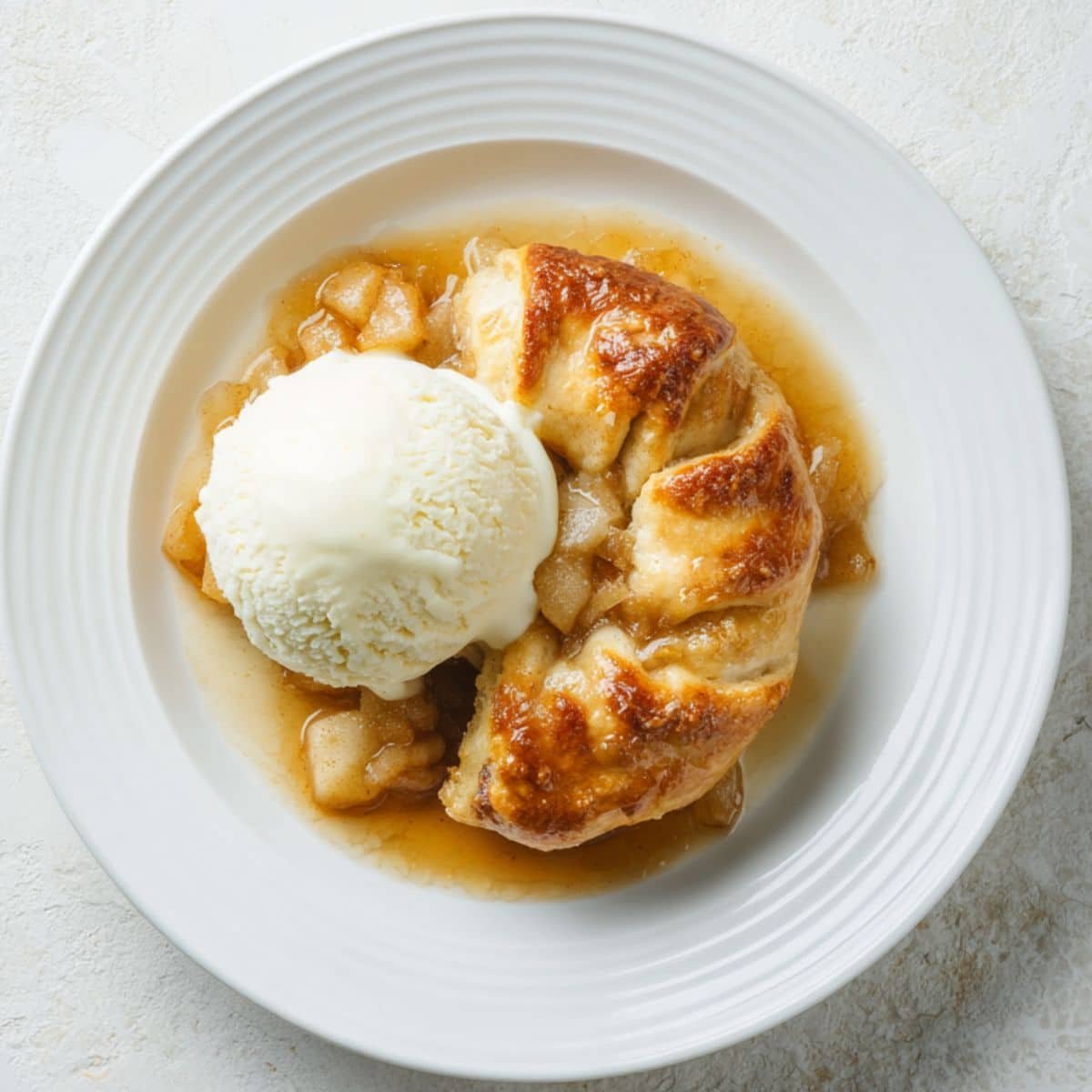 Freshly baked homemade apple dumplings in a white baking dish with buttery cinnamon sauce on a white kitchen counter