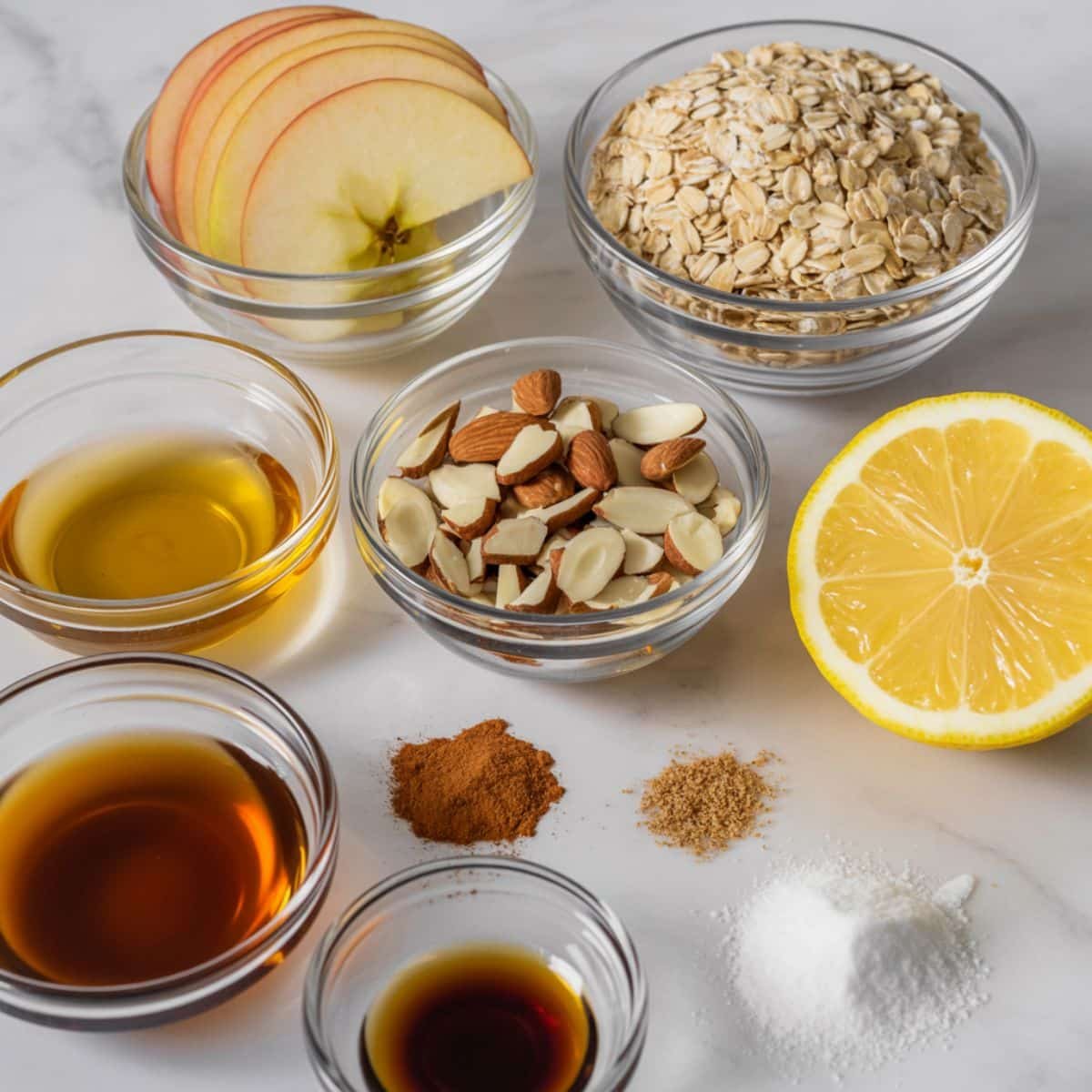 Healthy apple crisp ingredients — apples, oats, almonds, maple syrup, and spices on a white counter.