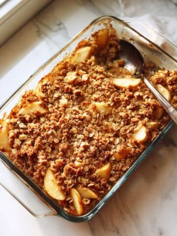 Healthy apple crisp ingredients — apples, oats, almonds, maple syrup, and spices on a white counter.