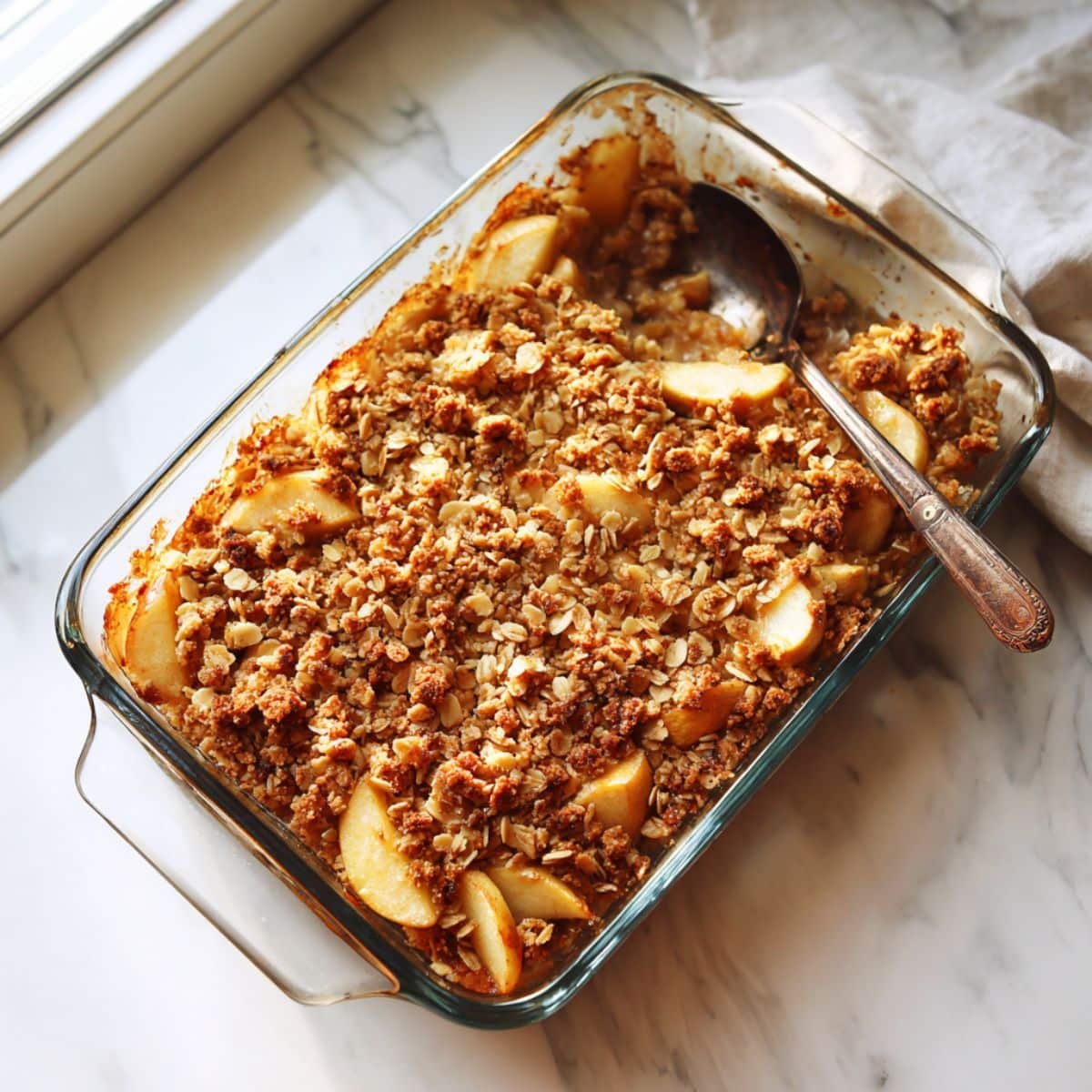 Healthy apple crisp ingredients — apples, oats, almonds, maple syrup, and spices on a white counter.