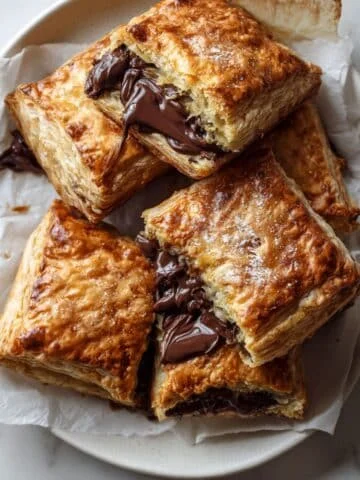 Top-down photo of freshly baked homemade chocolate pastry on a white kitchen table, golden and flaky with melted dark chocolate filling.