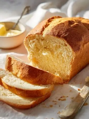 Homemade gluten free potato bread loaf sliced on a white kitchen table, showing soft texture and golden crust.