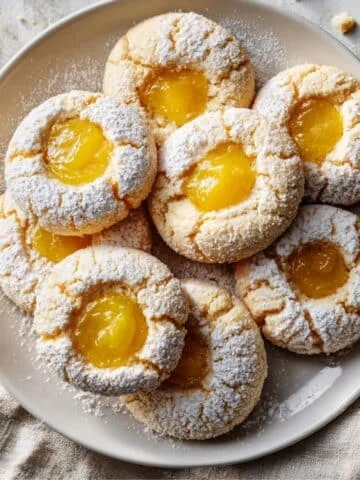 Top-down photo of homemade lemon curd cookies filled with lemon curd and dusted with powdered sugar on a white kitchen table.